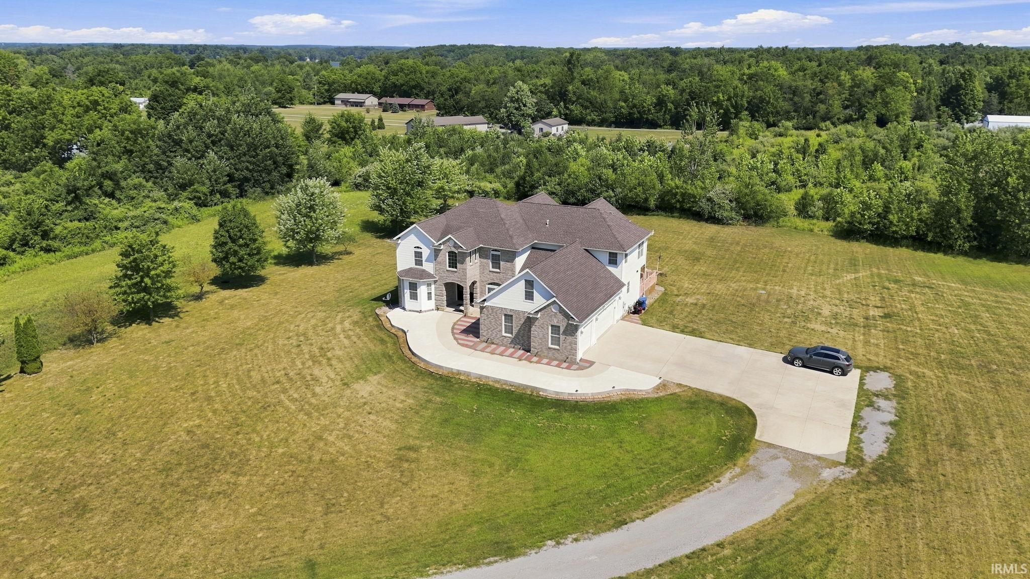 Large multi-story home on a spacious grassy lot, viewed from above with woodland behind it.