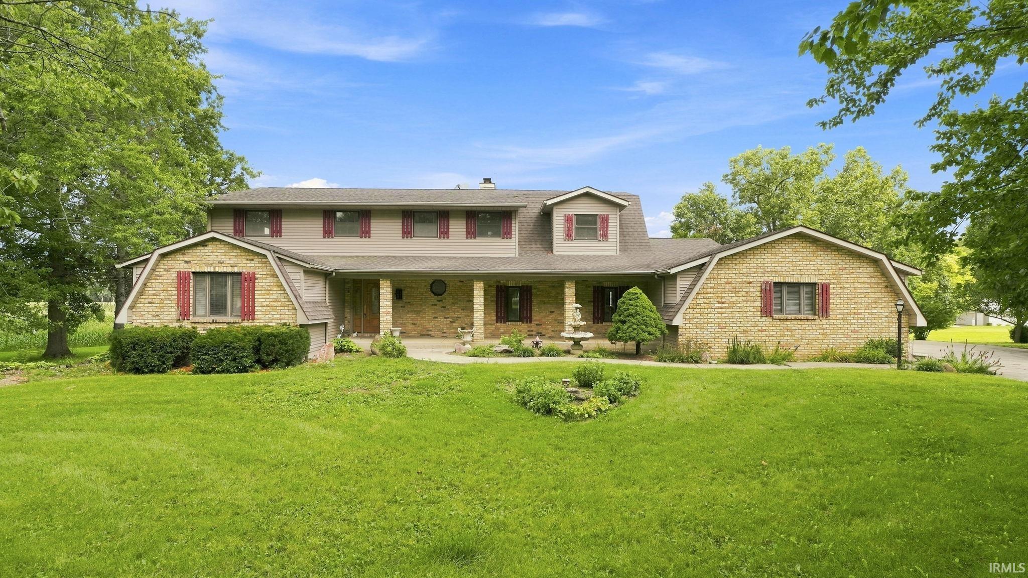 Large brick-and-siding home with red shutters, a landscaped entrance, and a wide green lawn.