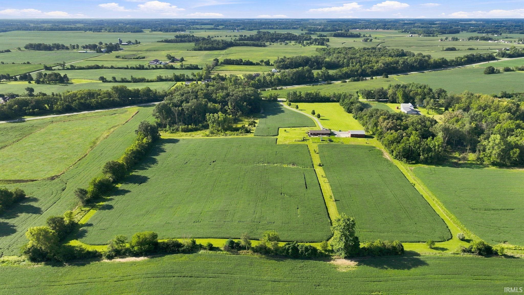 Aerial view of green farmland with scattered homes, barns, tree lines, and country roads.