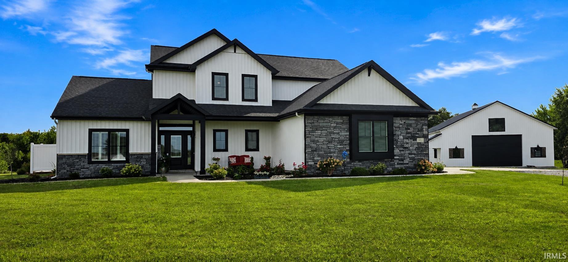 Two-story white home with dark trim and stone accents, beside a detached garage and broad lawn.