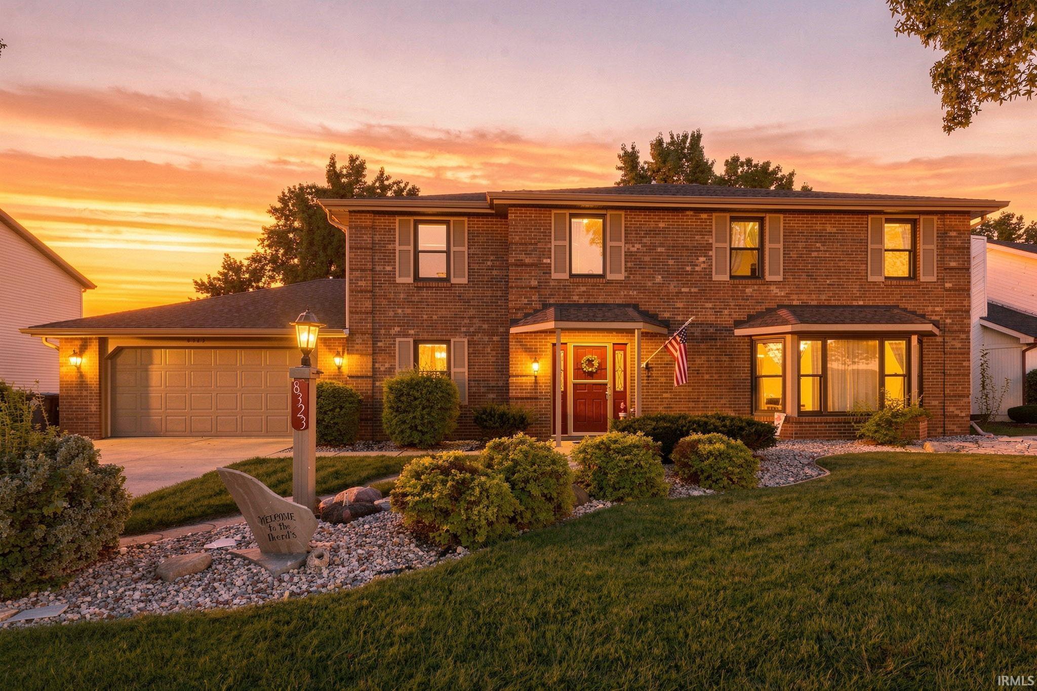 Two-story brick home with an attached garage and landscaped yard glowing in the sunset.