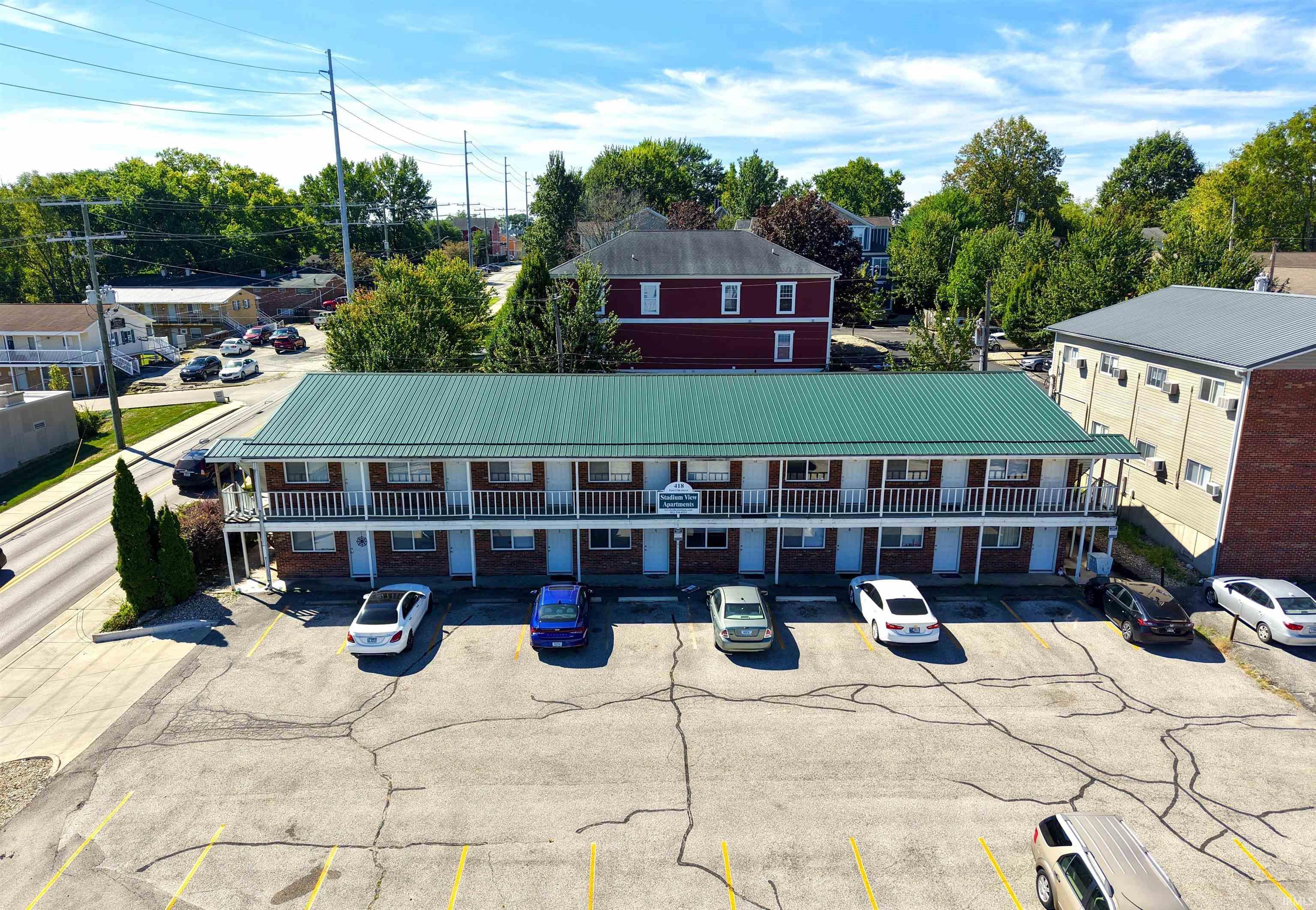Two-story brick apartment building with green roof, balcony walkways, and a parking lot.