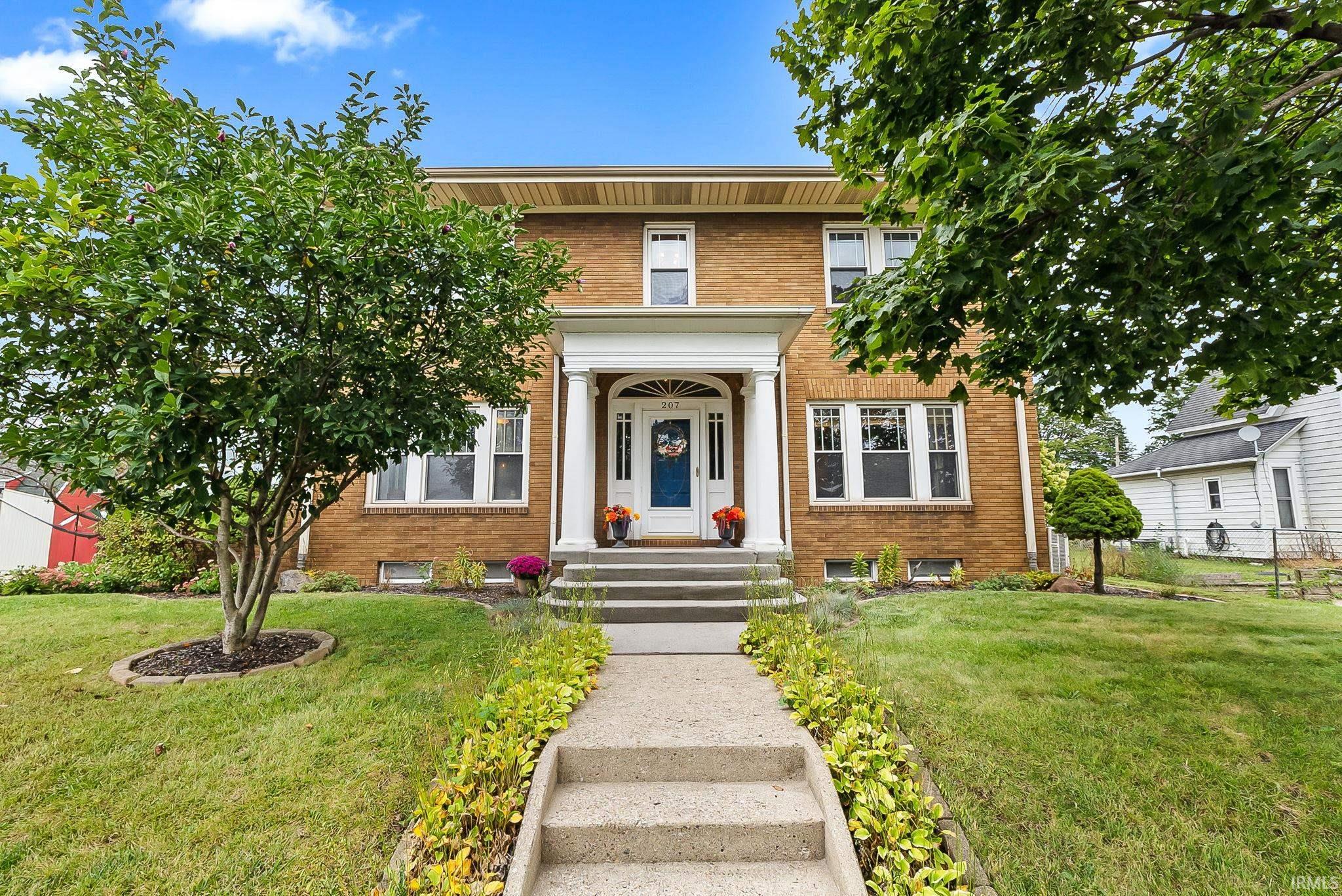 Two-story brick house with a white columned entry, concrete steps, and a landscaped front lawn.