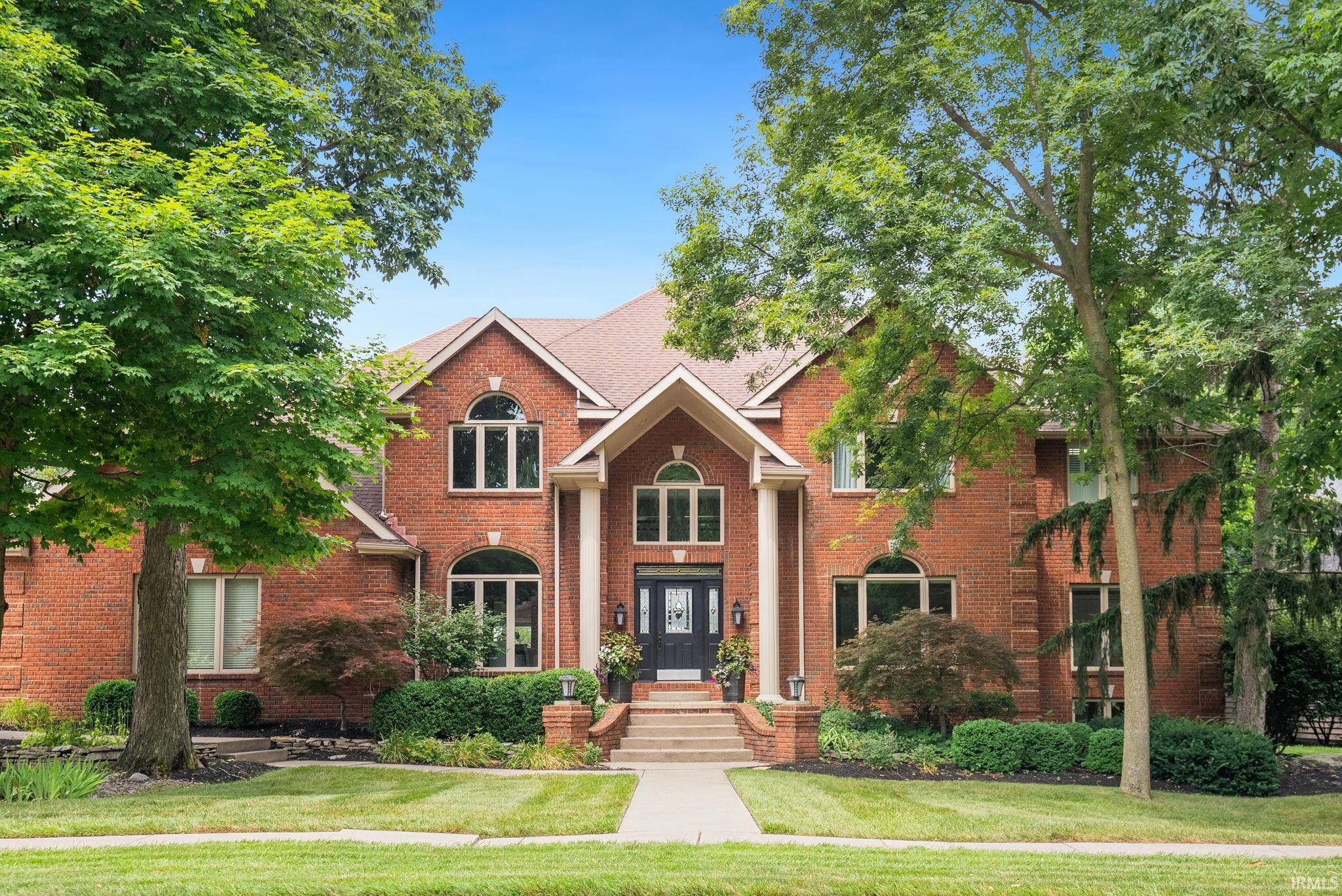 Two-story red brick house with arched windows, a covered entrance, and mature trees.