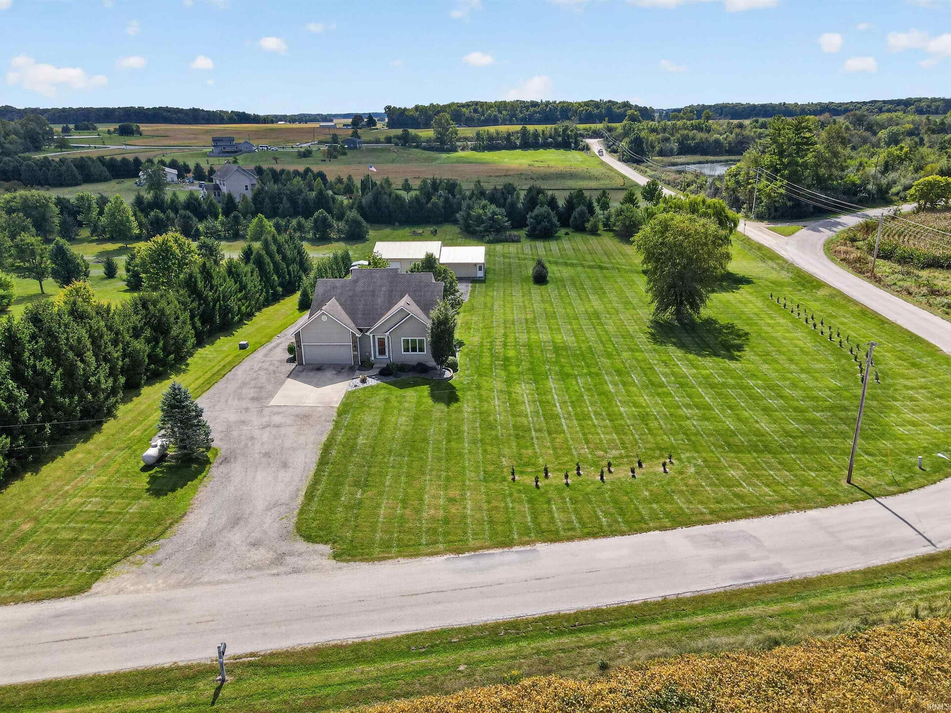 Aerial view of a gray house with a broad striped lawn, long driveway, and detached outbuilding.