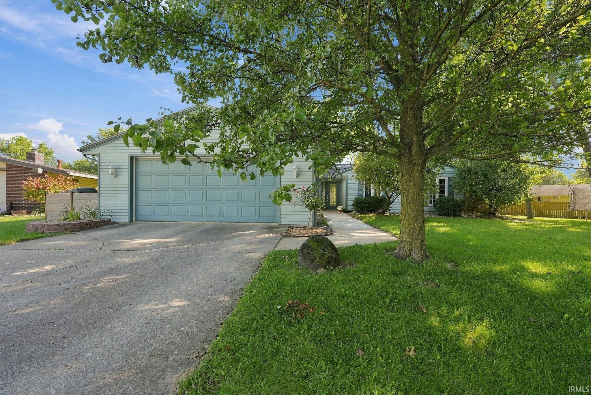Light blue-gray house with a wide driveway and two-car garage beneath a large leafy tree.