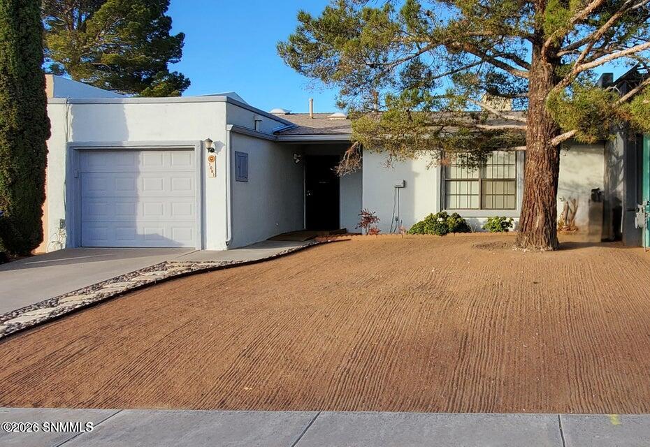 Single-story stucco home with an attached garage, gravel yard, and mature trees.