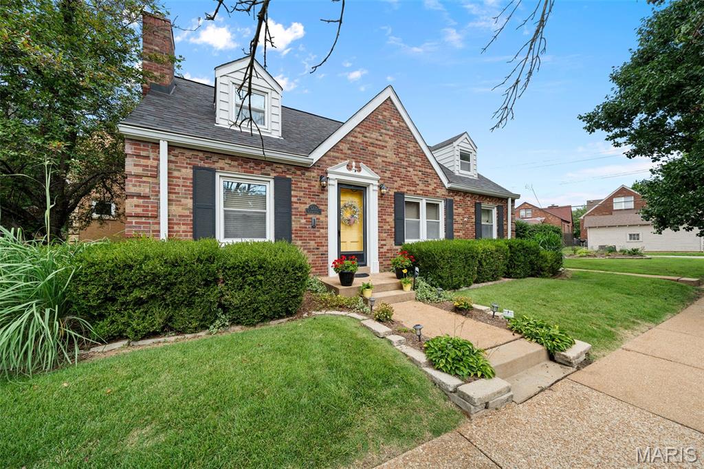 Red brick house with white dormers, dark shutters, and a yellow front door.