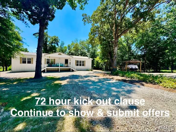 Single-story home beneath mature trees, with gravel drive and a 72-hour kick-out clause notice.