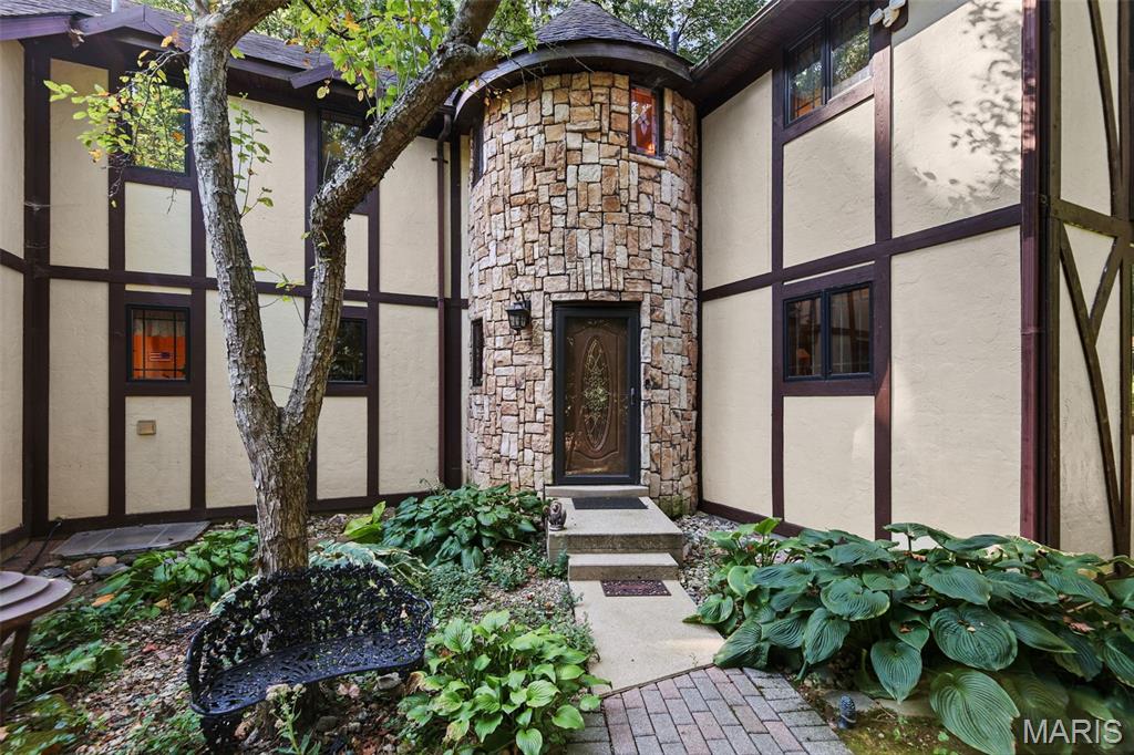 Tudor-style home entrance with a rounded stone tower, mature tree, and landscaped courtyard.