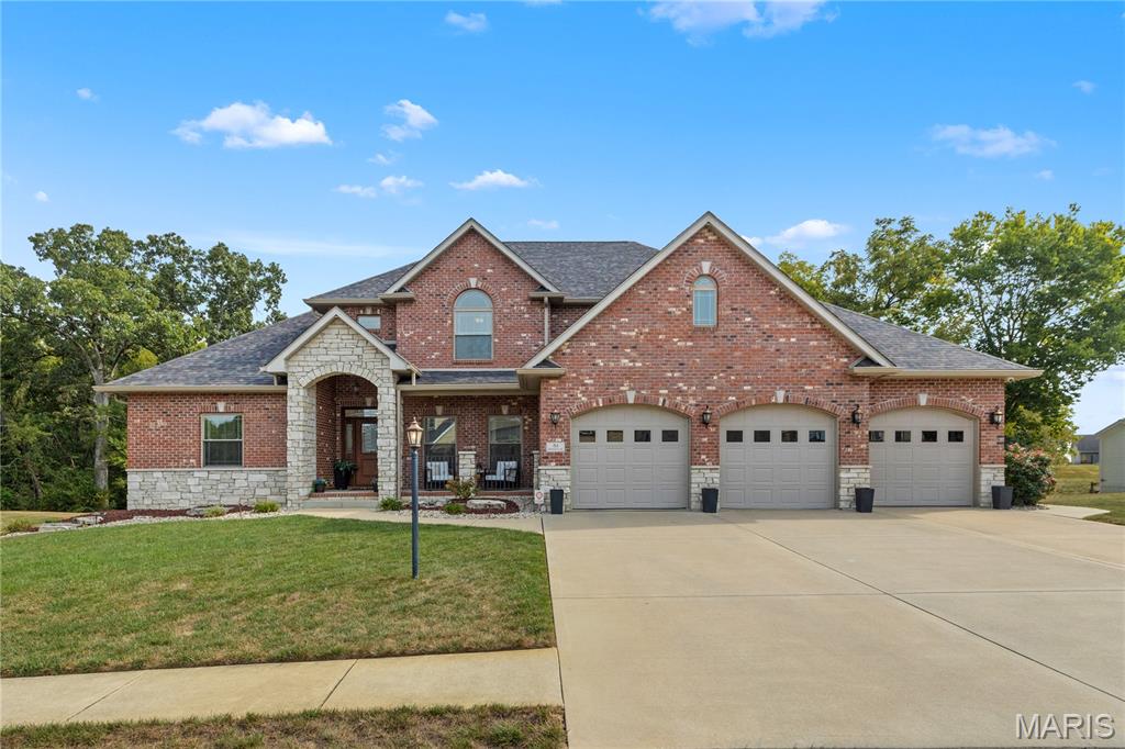 Two-story brick home with stone accents, three garage doors, and a wide driveway.