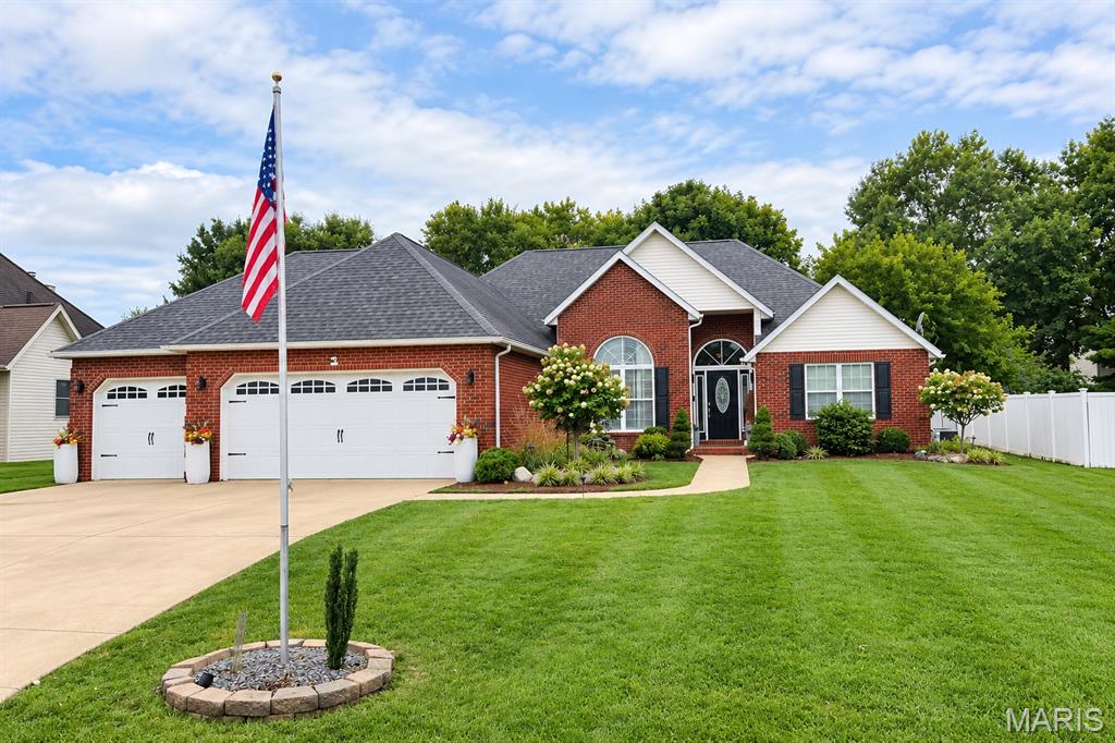 Red-brick home with a two-car garage, landscaped lawn, and American flag.