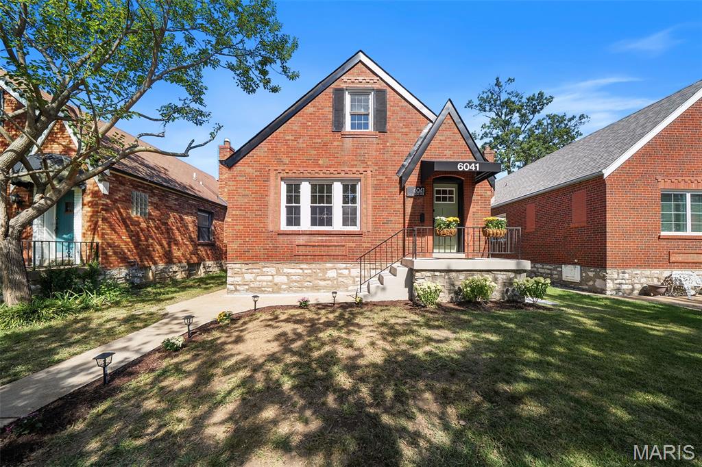 Red-brick gabled house with a stone foundation, covered entry, and shaded front lawn.