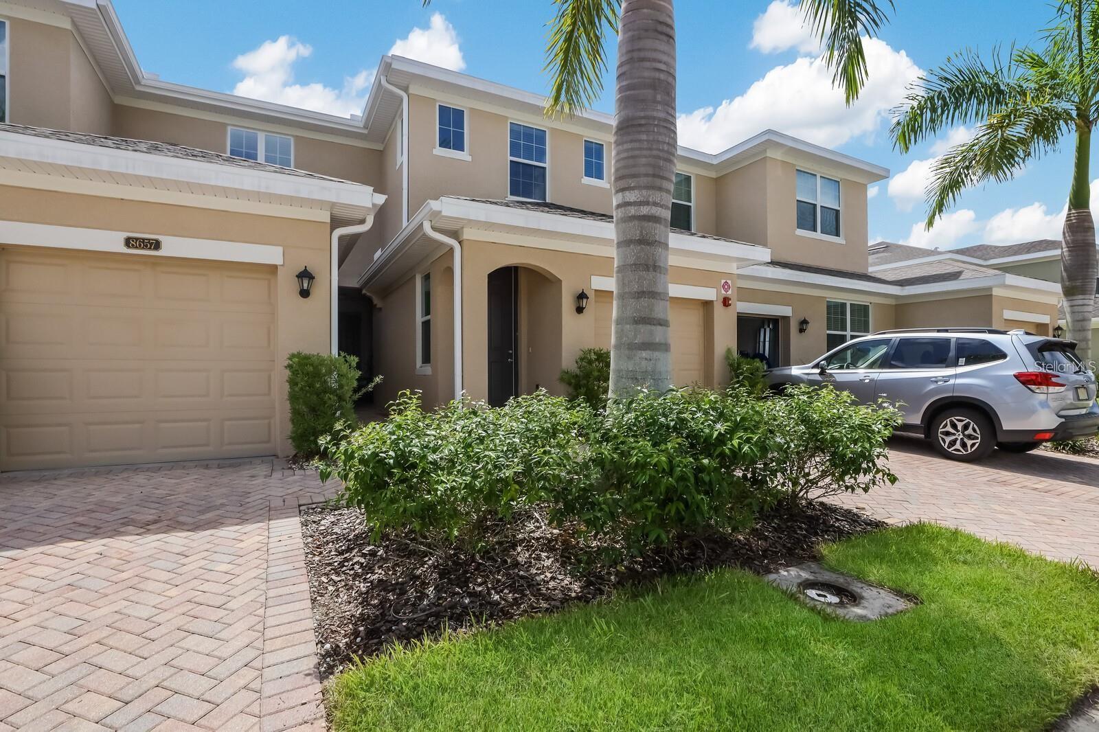 Beige multi-story townhouse with a garage, palm trees, and a silver SUV in the driveway.