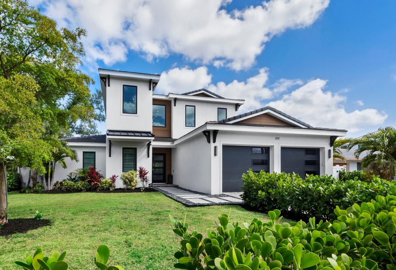 Modern two-story white home with a dark double garage and tropical landscaping.