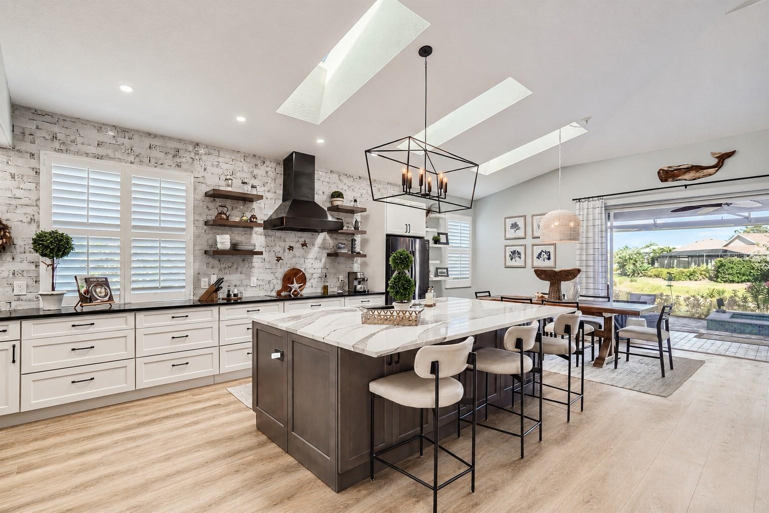 Open-plan kitchen with a large island, white cabinets, skylights, and patio access.