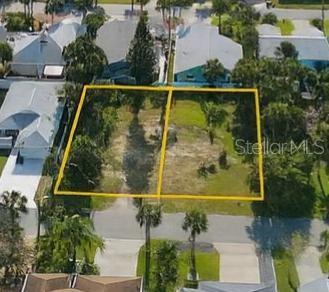 Vacant residential lot outlined in yellow, with trees and cleared ground among neighboring homes.