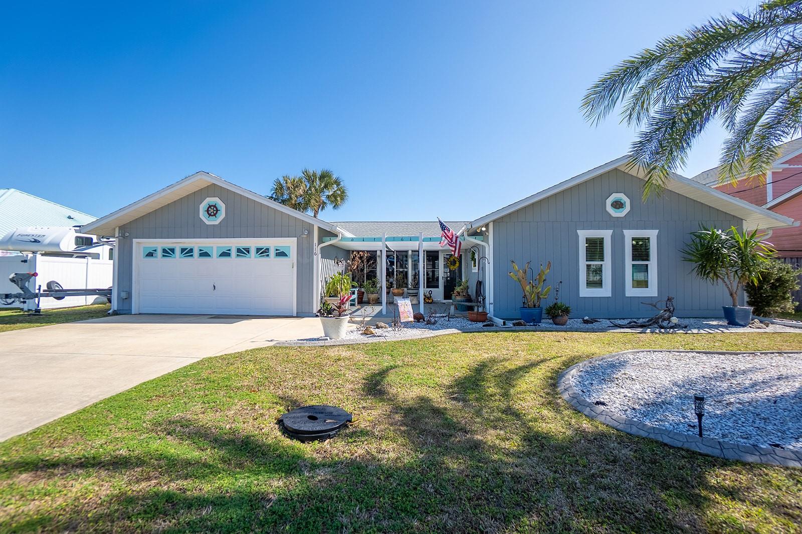 Blue-gray coastal home with a two-car garage, covered entry, and palm landscaping.