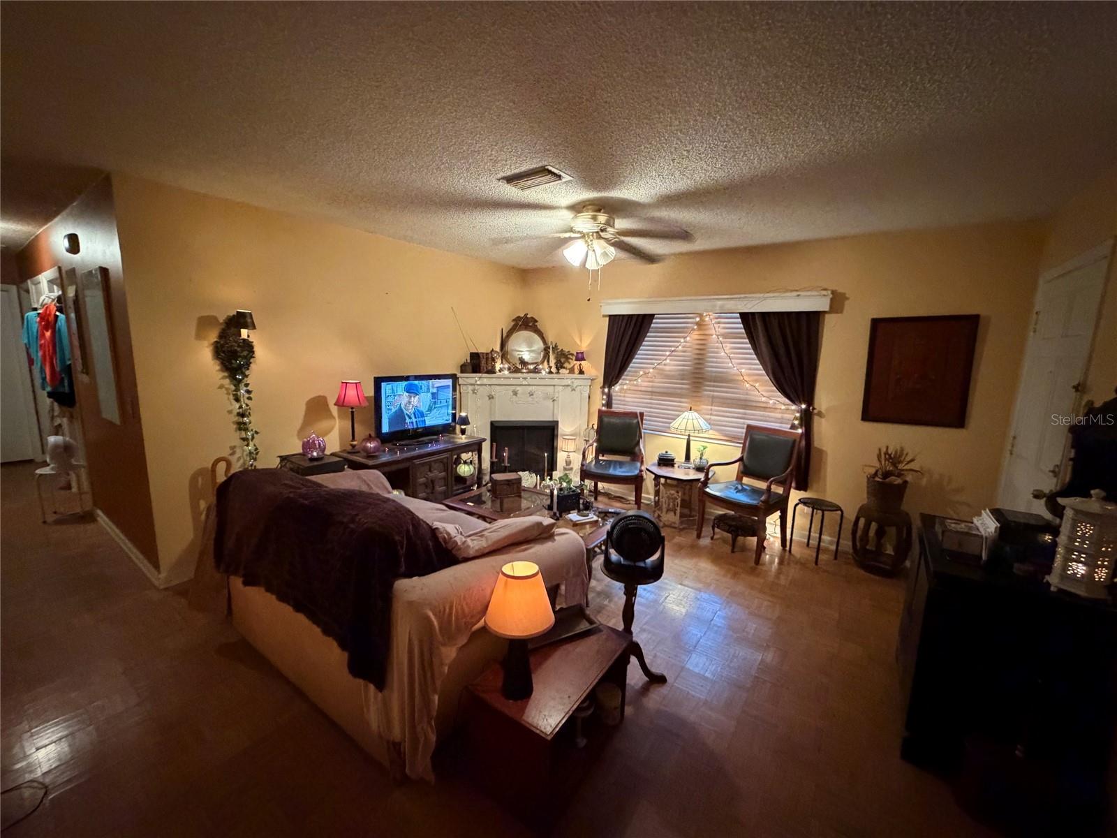 Furnished living room with a white fireplace, sofa, armchairs, and curtained window.