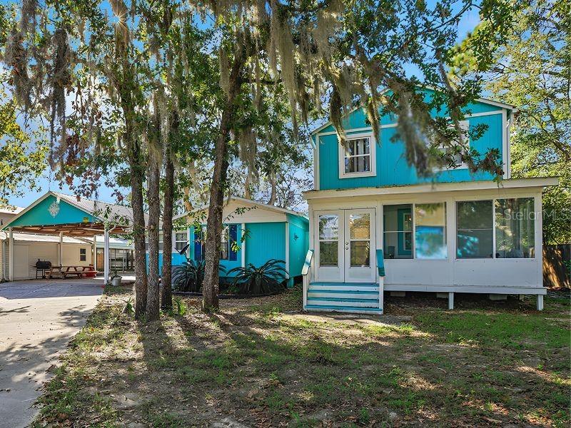 Turquoise two-story home with an enclosed porch and covered carport beneath mature moss-draped trees.