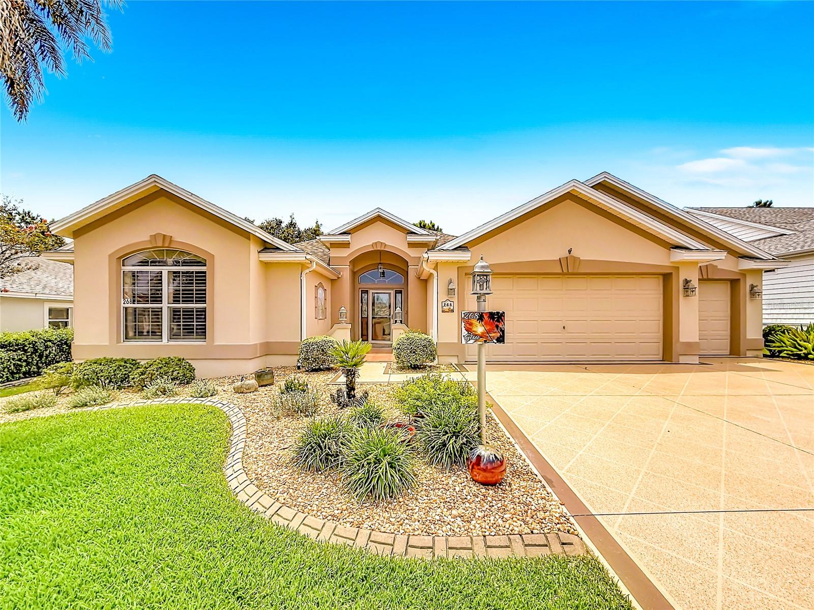 Single-story peach home with a two-car garage, tiled driveway, and landscaped front yard.