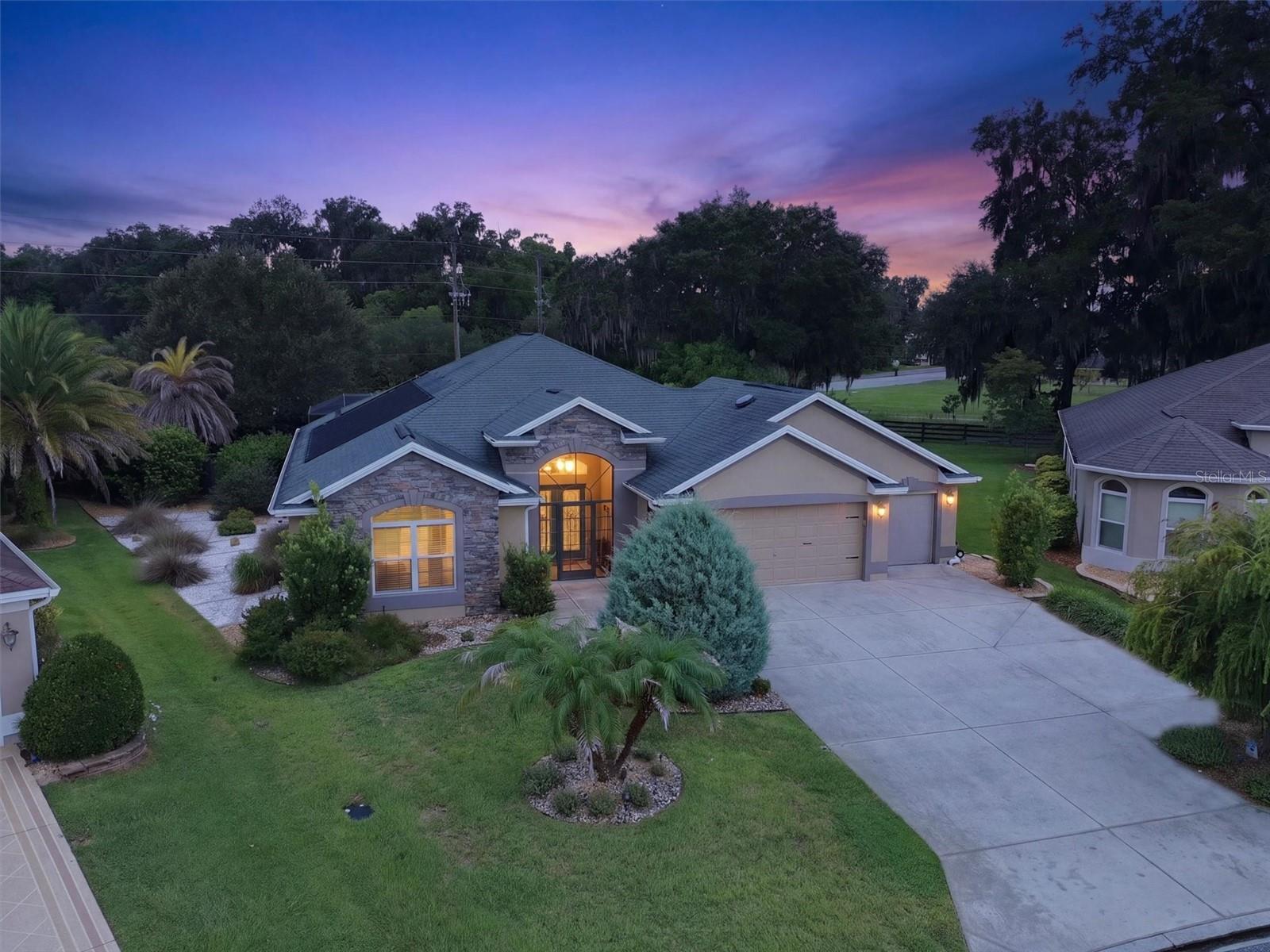 Single-story home with a stone-accented facade and broad driveway beneath a purple-pink dusk sky.