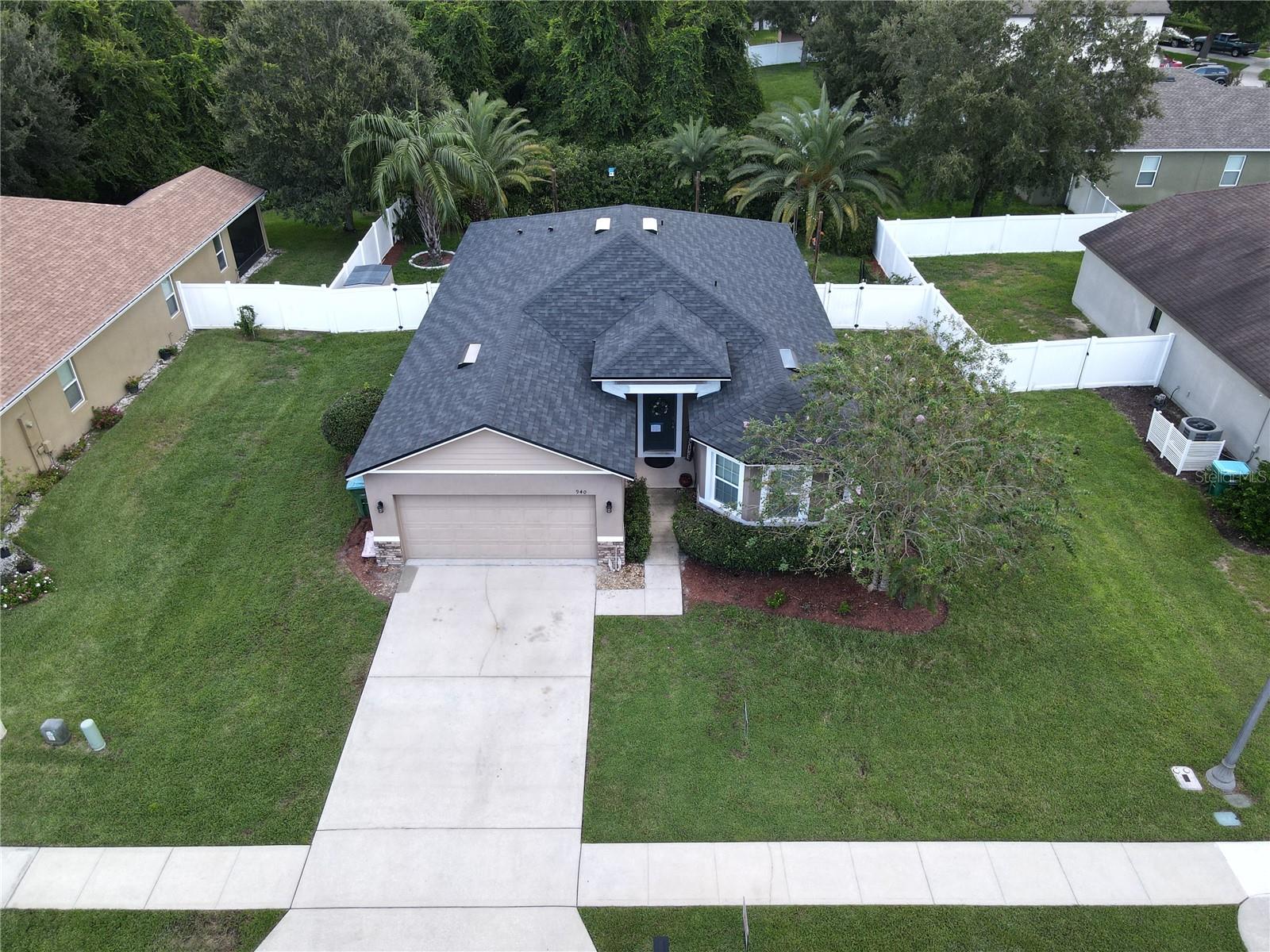 Aerial view of a single-story home with a gray roof, two-car garage, driveway, and fenced backyard.