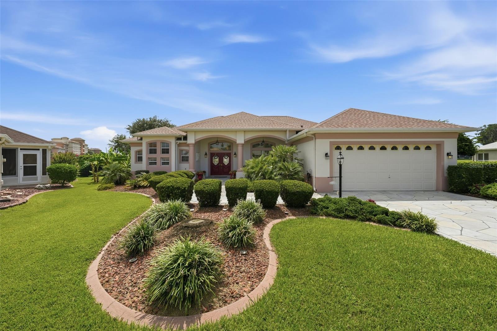 Single-story home with a two-car garage, arched entry, red double doors, and landscaped front yard.