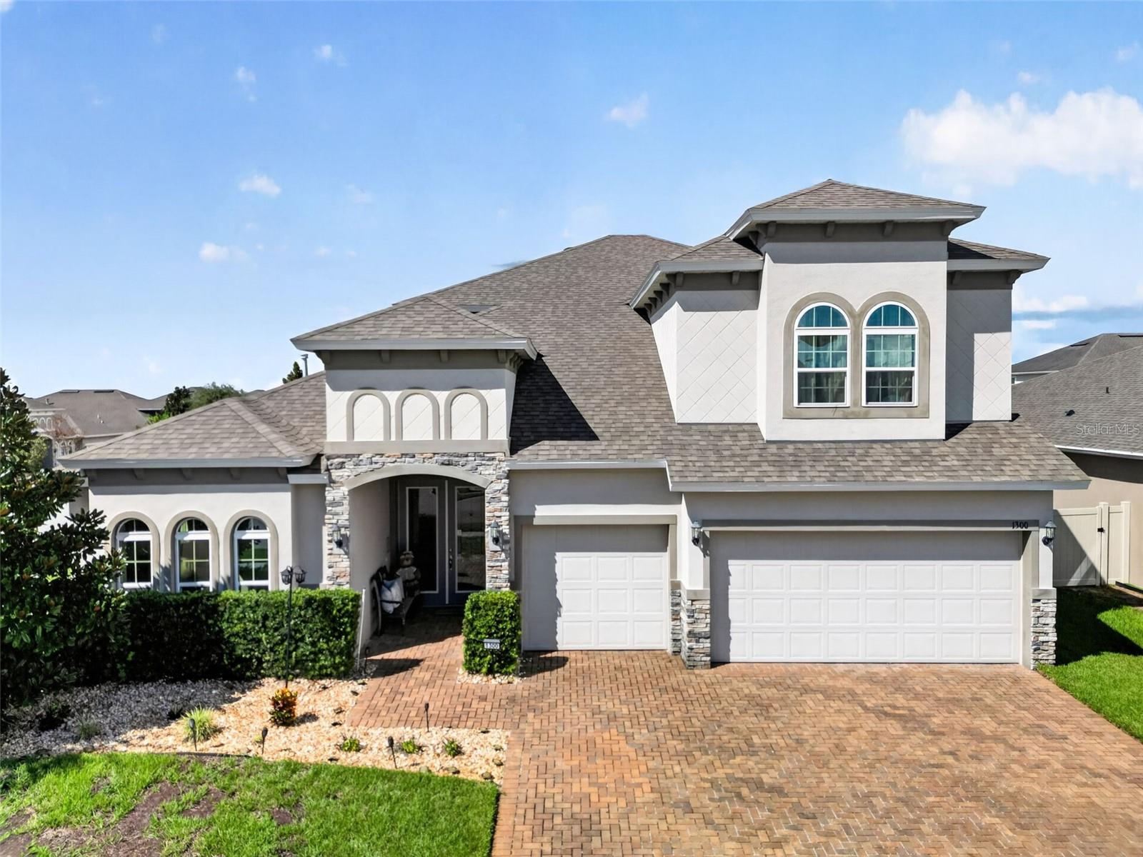 Two-story home with arched windows, stone accents, a three-car garage, and brick-paver driveway.