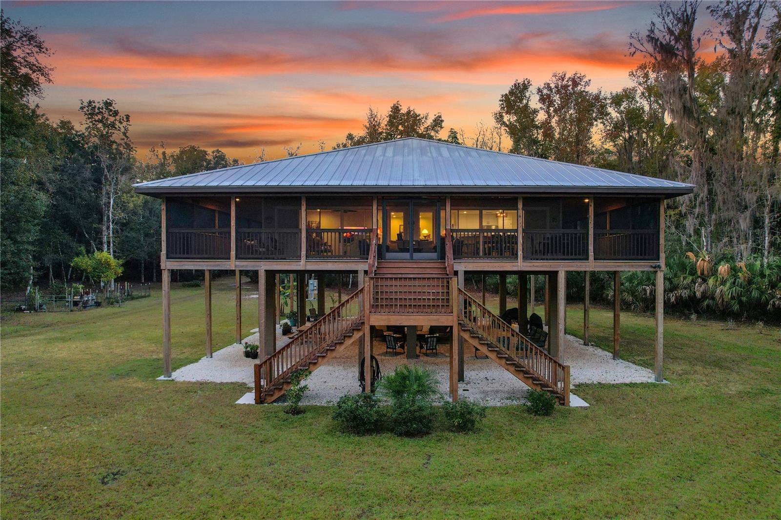 Elevated wood home with a metal roof and wide screened porch at sunset.