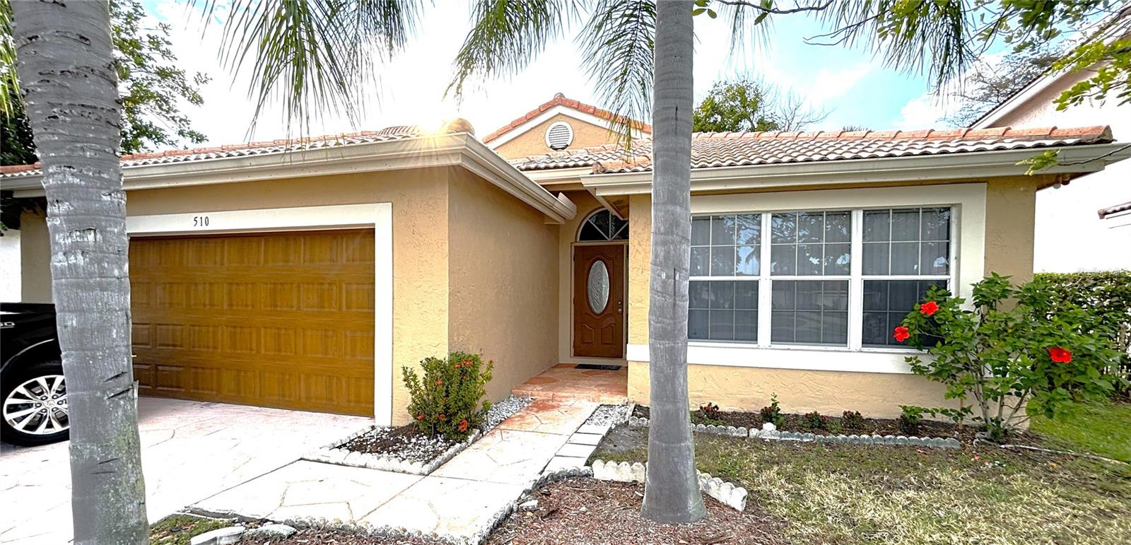 Tan stucco house with a wooden garage door, tiled roof, and palm trees in front.