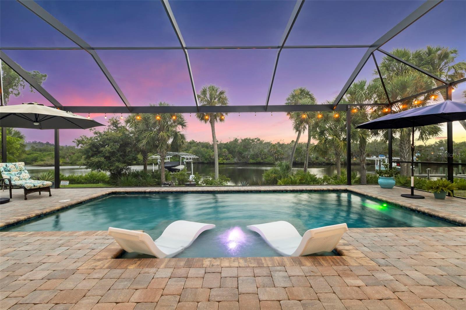 Backyard pool with in-water loungers and a screened lanai overlooking the water at dusk.