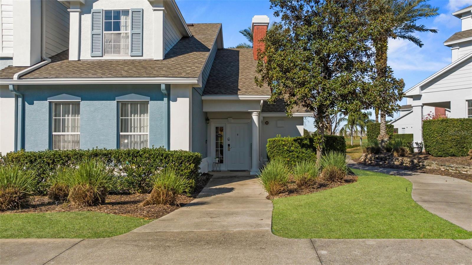 Two-story blue-gray home with a covered entry, landscaped lawn, and neighboring homes.