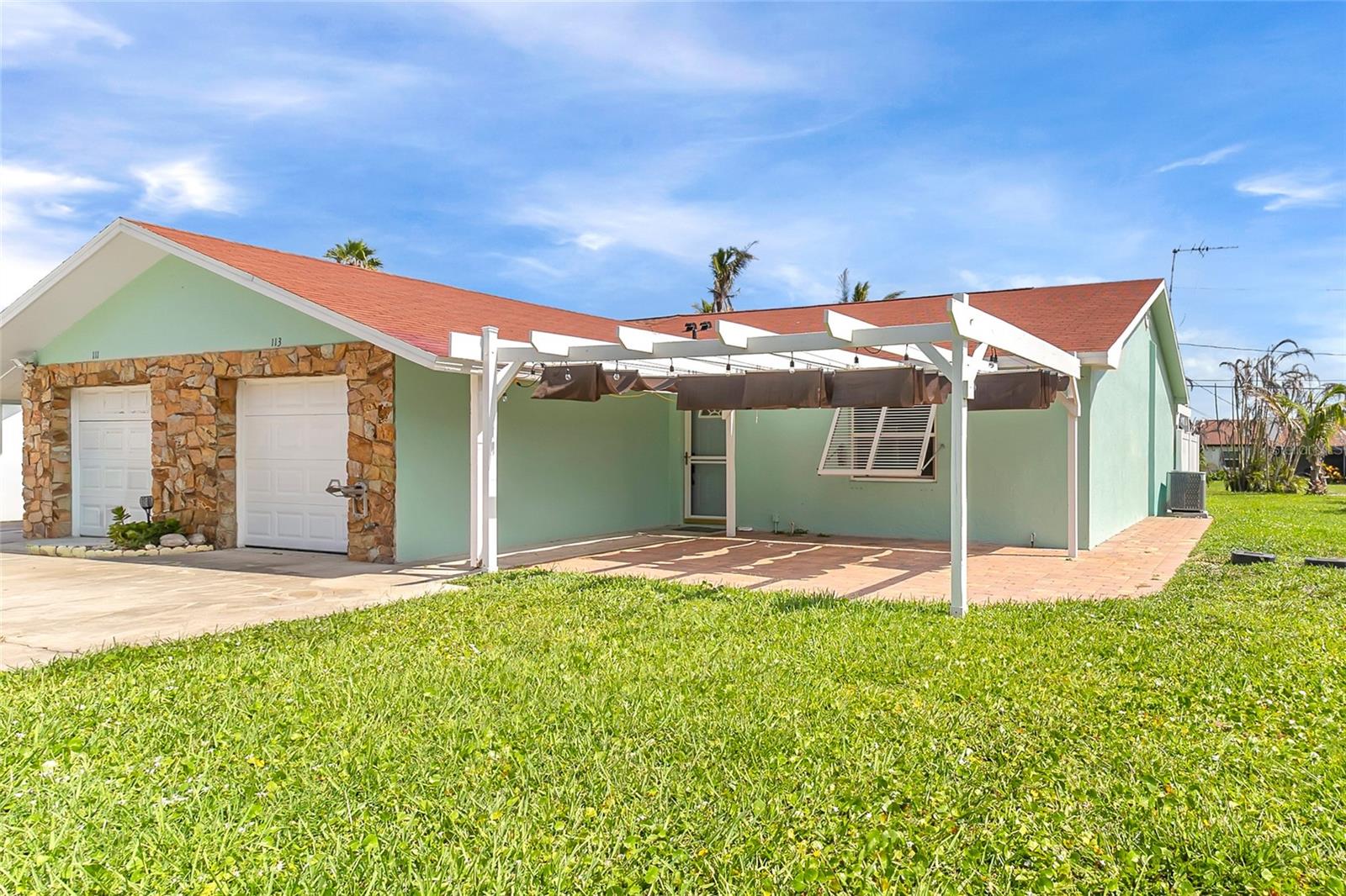 Mint-green single-story house with a stone-front garage and white pergola-style carport over the patio.