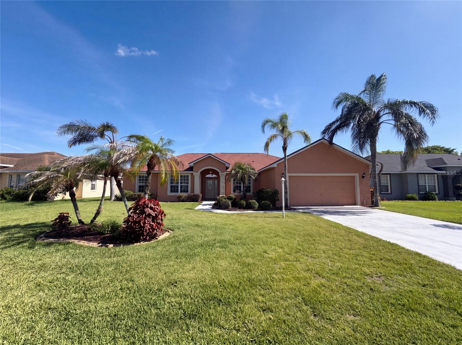 Terracotta single-story home with a red roof, arched entry, two-car garage, and palm trees.