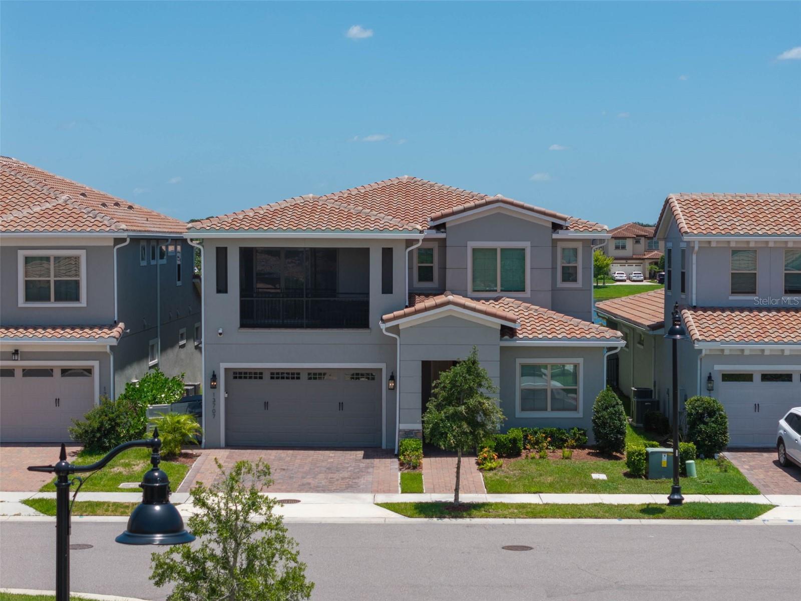 Gray two-story home with a screened balcony and terracotta roof, among similar neighborhood houses.