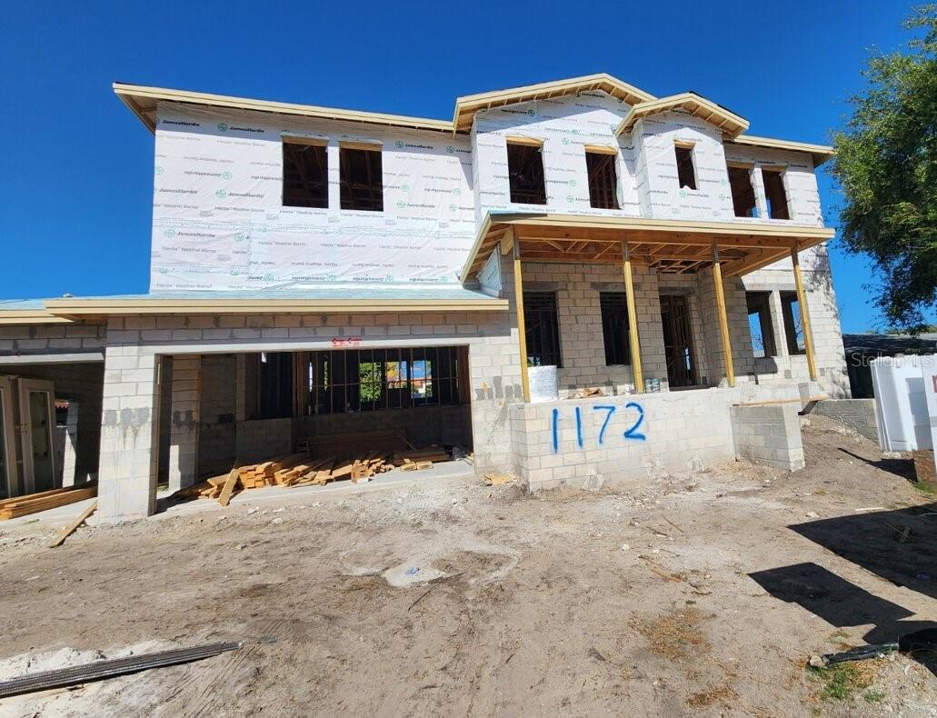Two-story house under construction, with exposed framing and 1172 painted on the front wall.