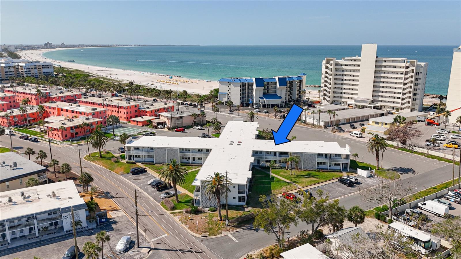 Low-rise co-op building marked by a blue arrow, with the beach and ocean behind it.