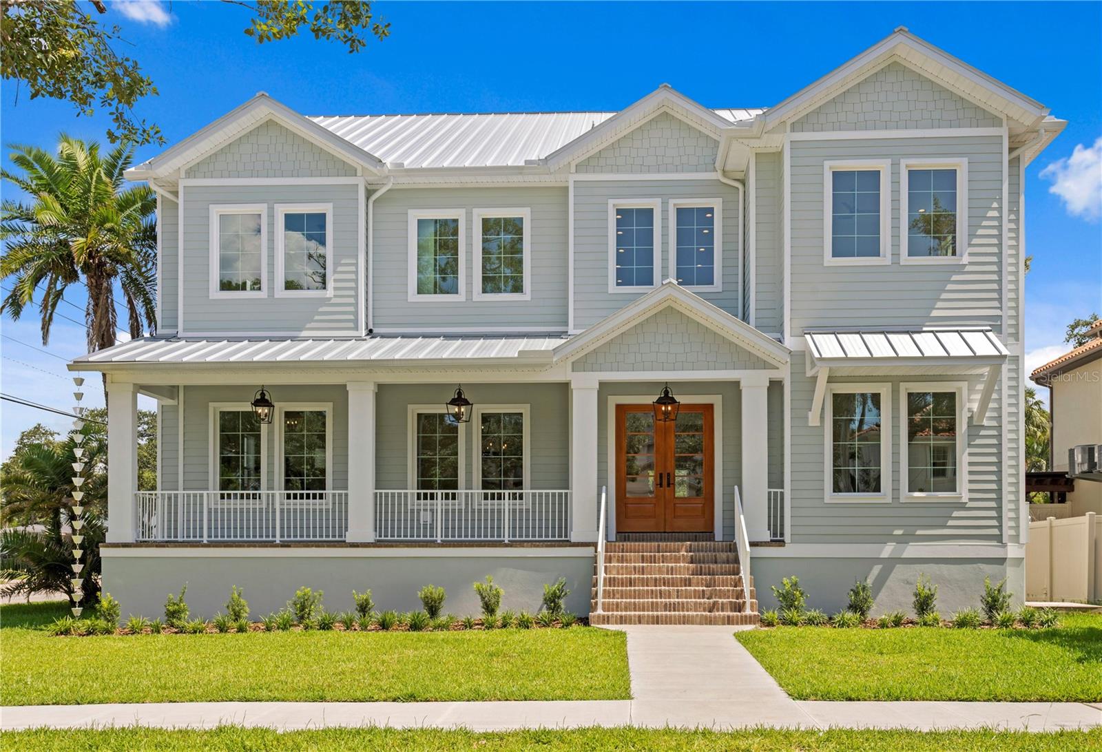 Two-story gray home with a white metal roof, covered porch, and brick front steps.
