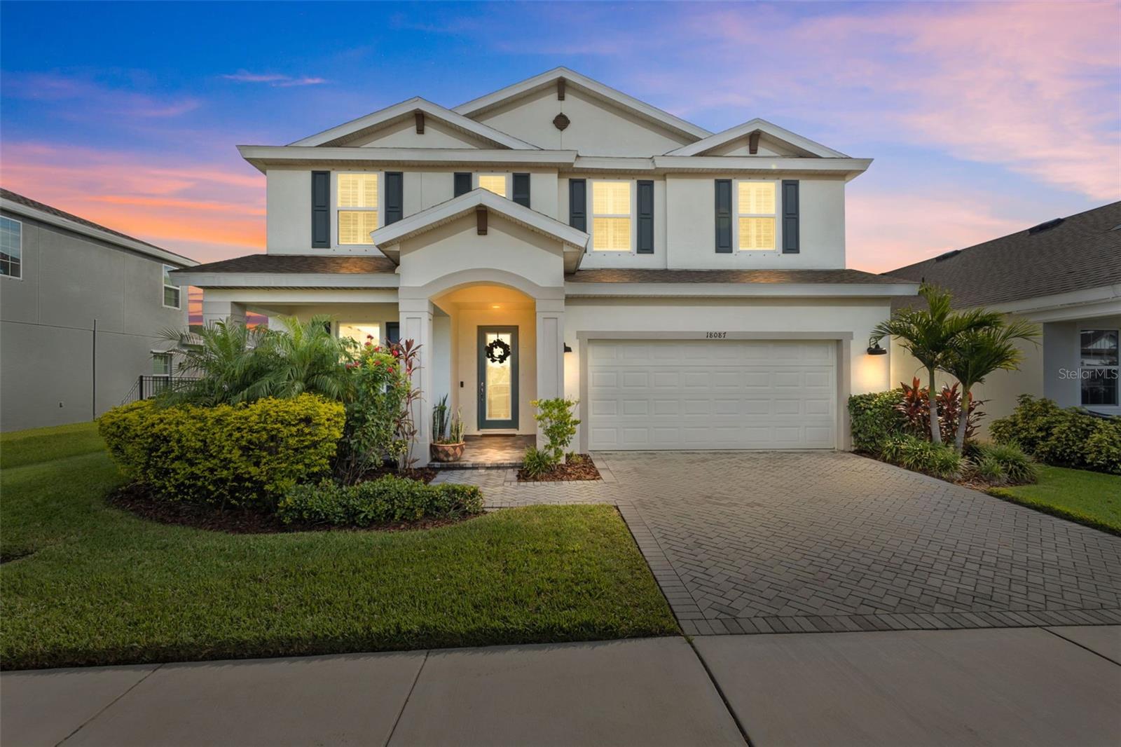 Two-story white house with a double garage and landscaped front yard at sunset.