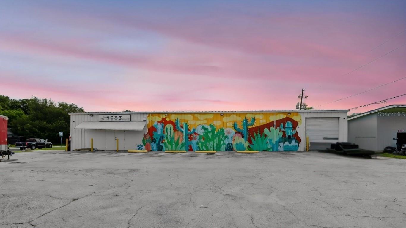 Commercial warehouse with a colorful facade mural and broad paved lot at dusk.