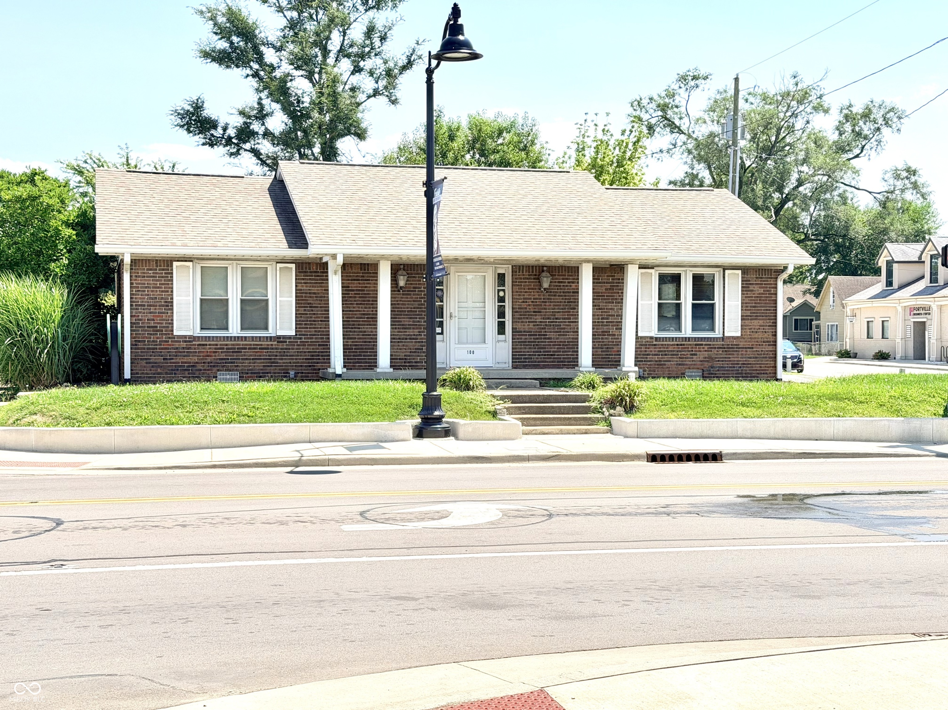 Single-story brick building with white trim, a centered entrance, and a black streetlamp out front.