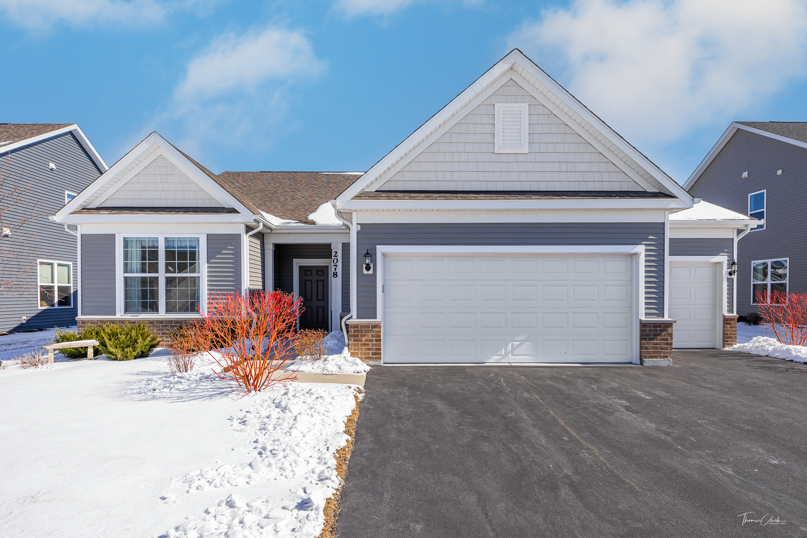 Gray single-story home with two garage doors and a snow-covered front yard.