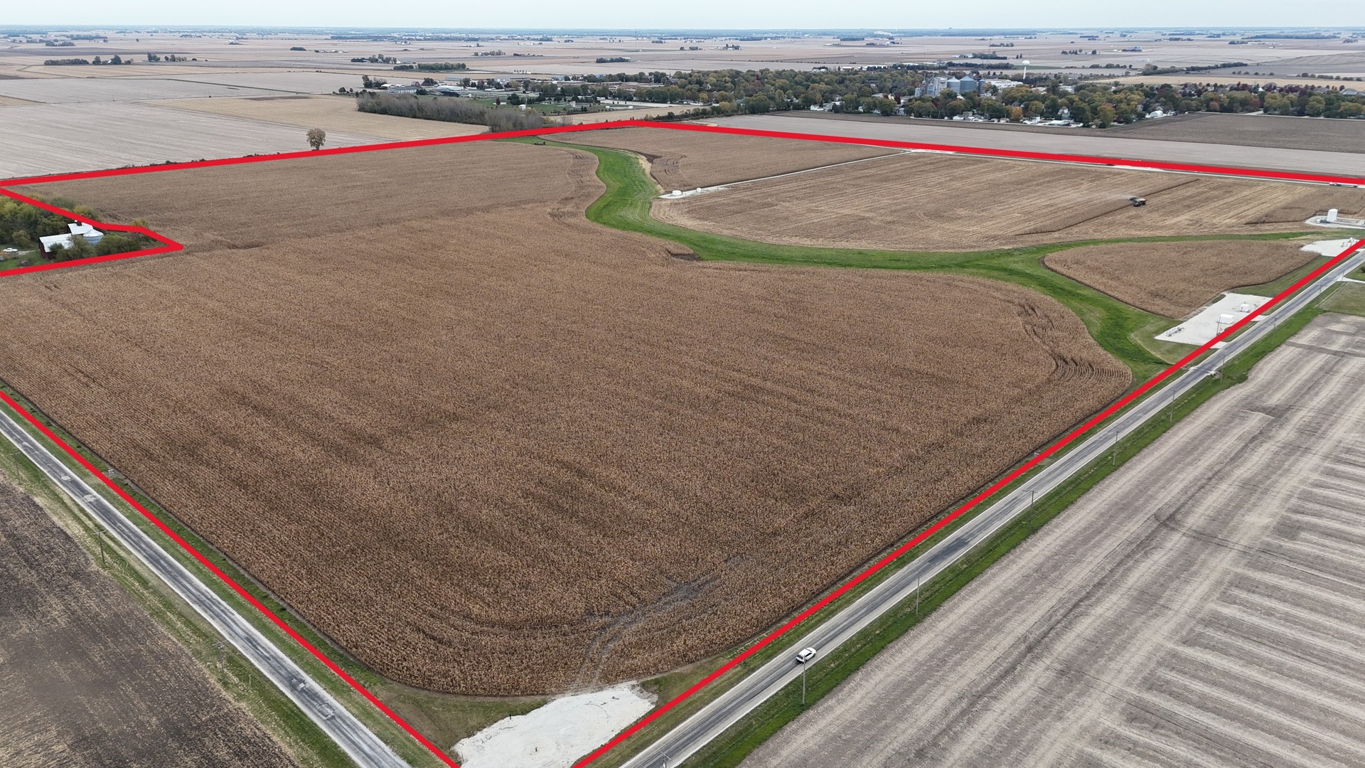 Aerial view of a large farm field outlined in red, with roads along two sides and a green drainage strip.