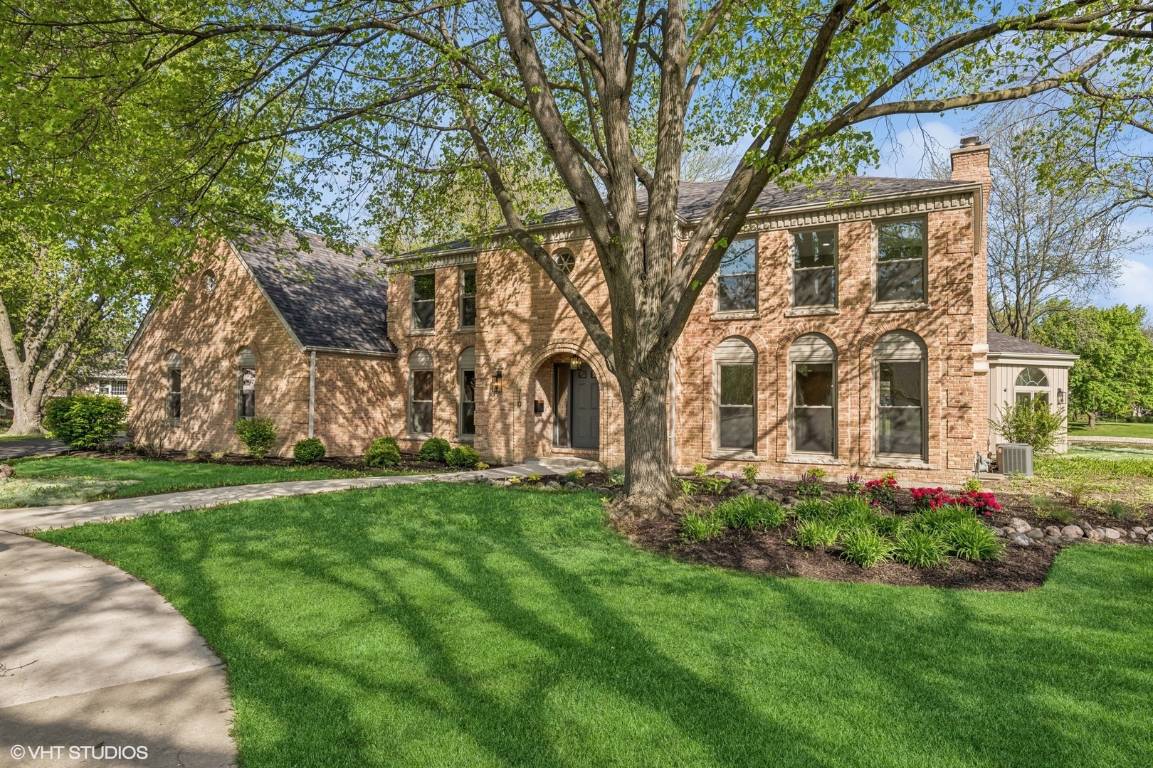 Two-story brick house with arched windows, a large shade tree, and landscaped lawn.