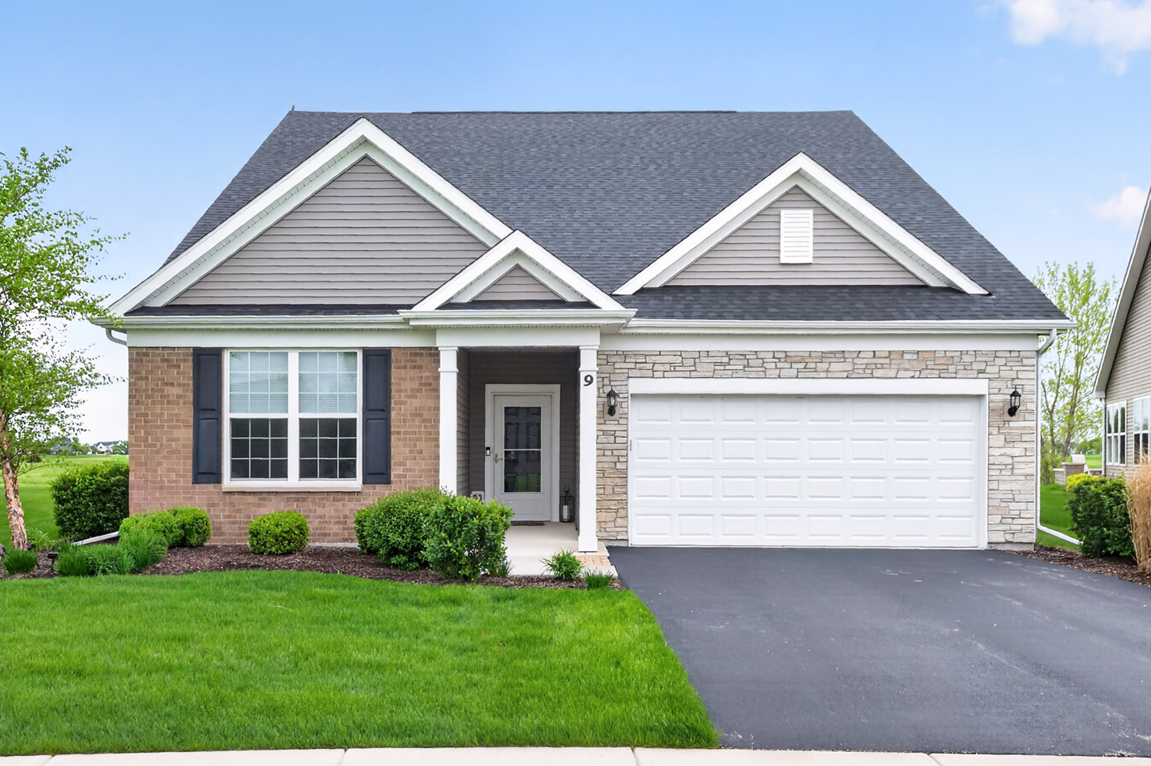 Single-story brick and stone home with a gabled roof, white two-car garage, and landscaped front lawn.