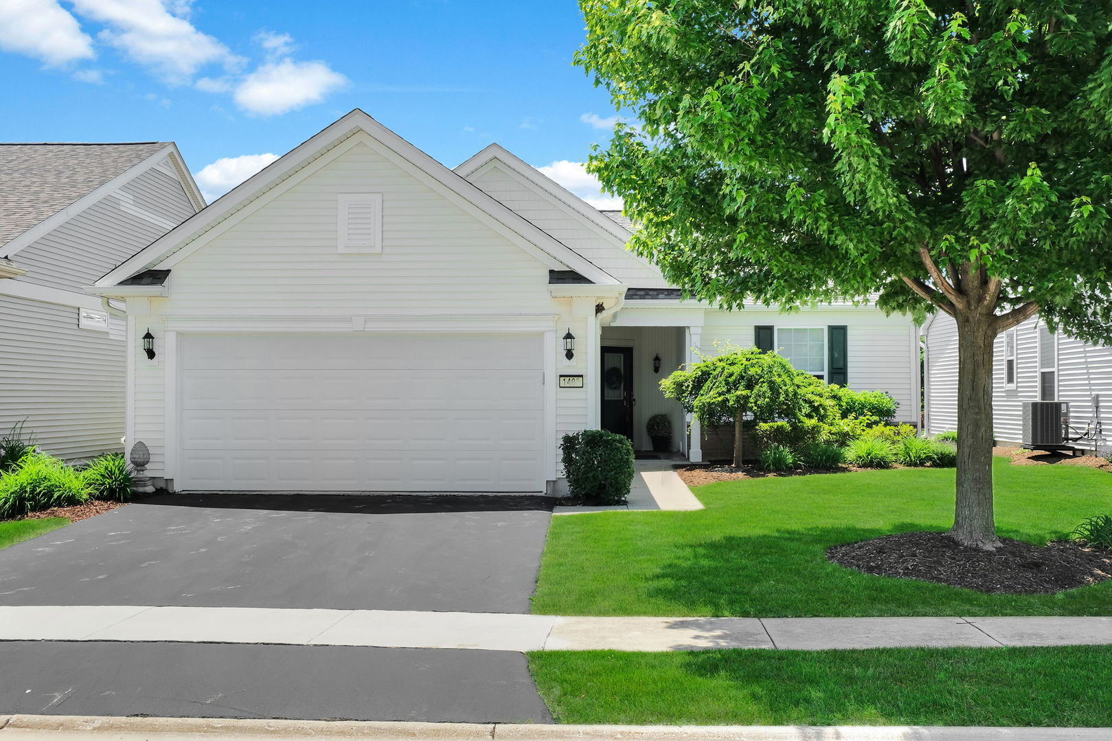 White single-story home with a two-car garage, covered entry, and large shade tree.
