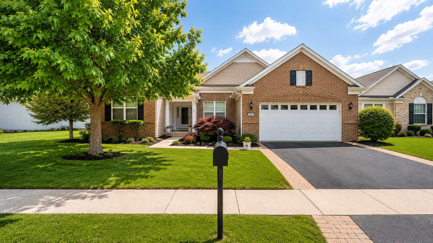 Brick ranch home with a white double garage, landscaped lawn, and large shade tree.