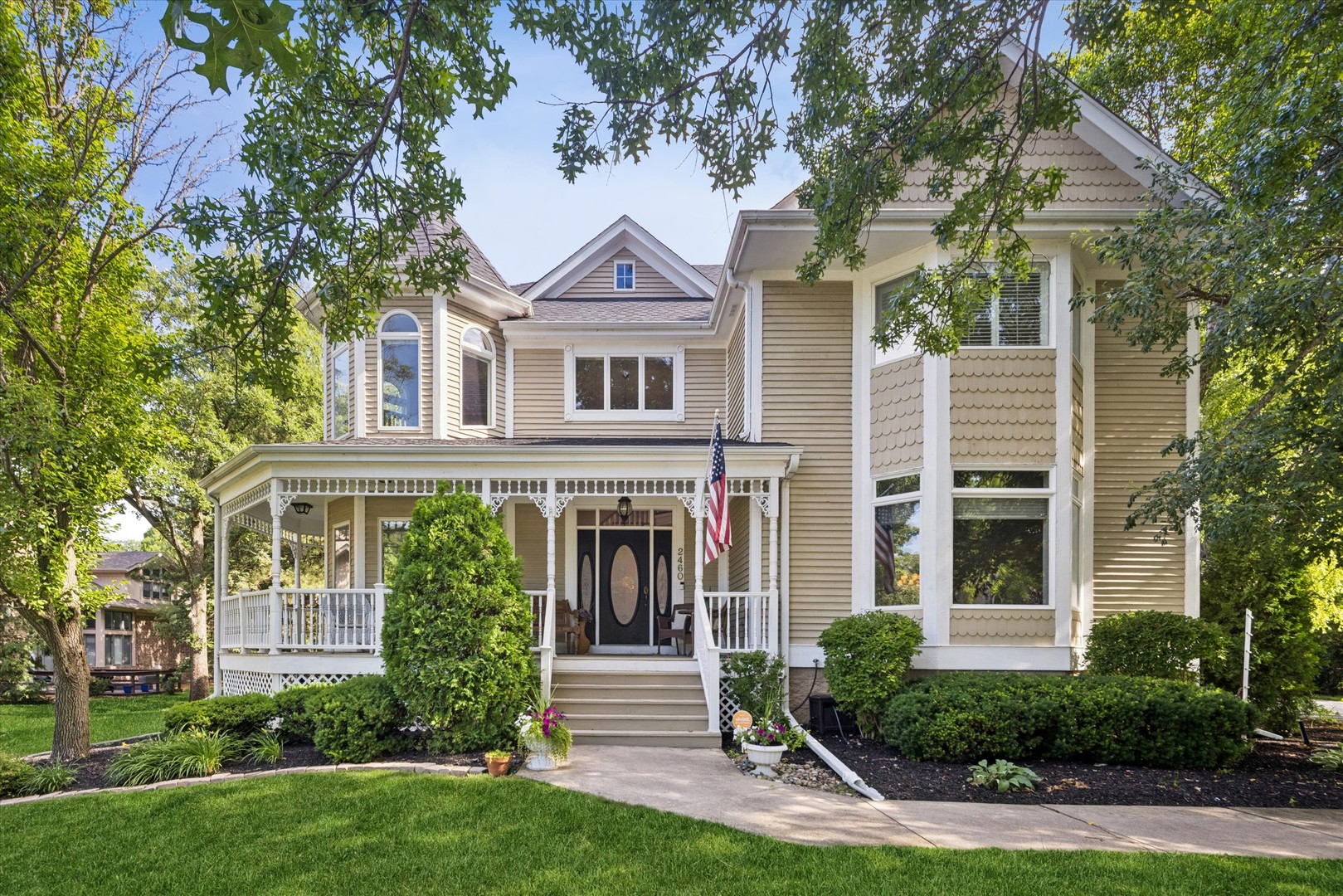 Beige two-story home with a covered porch, bay window, and mature trees.