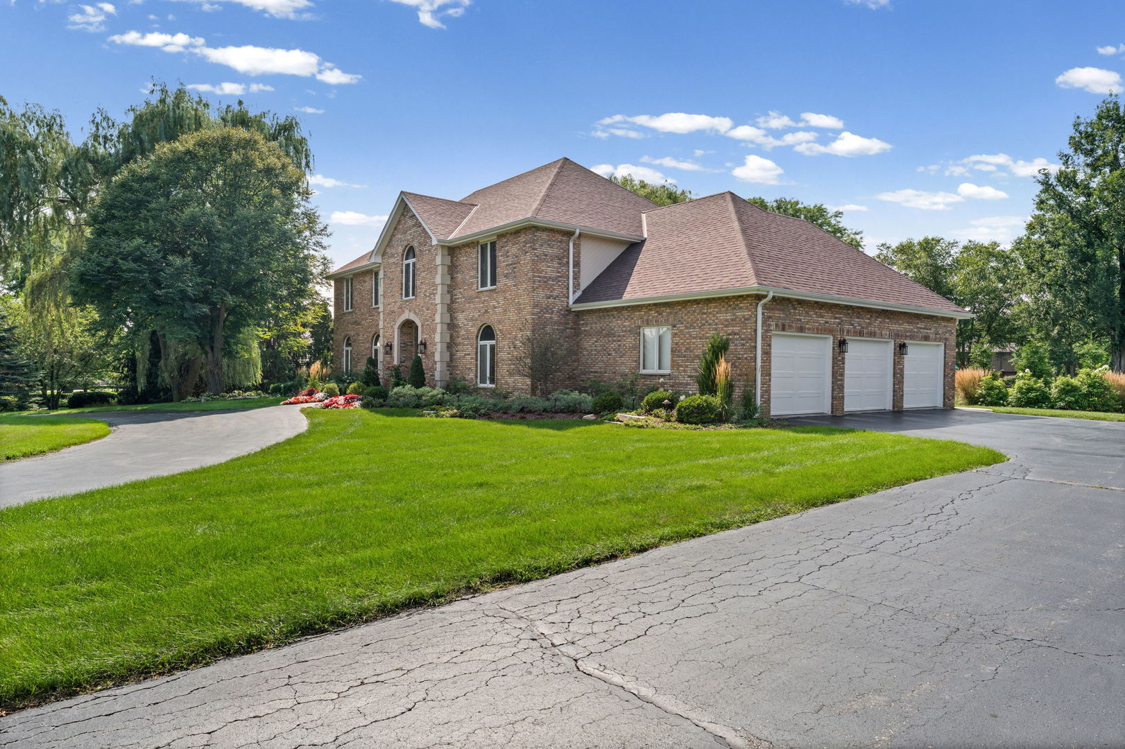 Two-story brick home with an arched entry, landscaped flower beds, and a curved driveway.